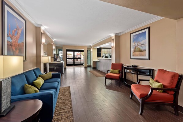 A spacious hotel lobby with a blue sofa, red armchair, and a small table. There is a kitchen area in the background. - Mainstay Suites El Centro I-8 (El Centro)