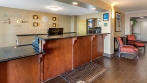 Un'area reception con scrivania in legno, un cartello con la scritta "MainStay Suites" e un'area salotto con sedie rosse.
