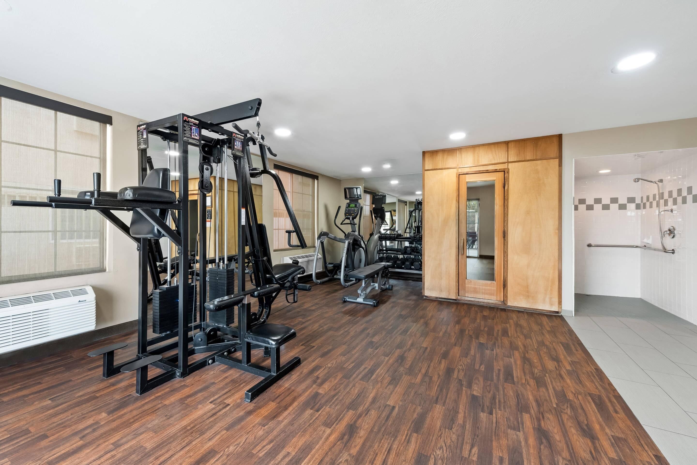Un gimnasio con equipamiento de ejercicio, suelo de madera y un espejo grande.