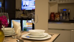 A dining table set with white plates, a wine glass, and a folded napkin. A television is mounted on the wall in the background. - TN & CO Hotel (Mugla)