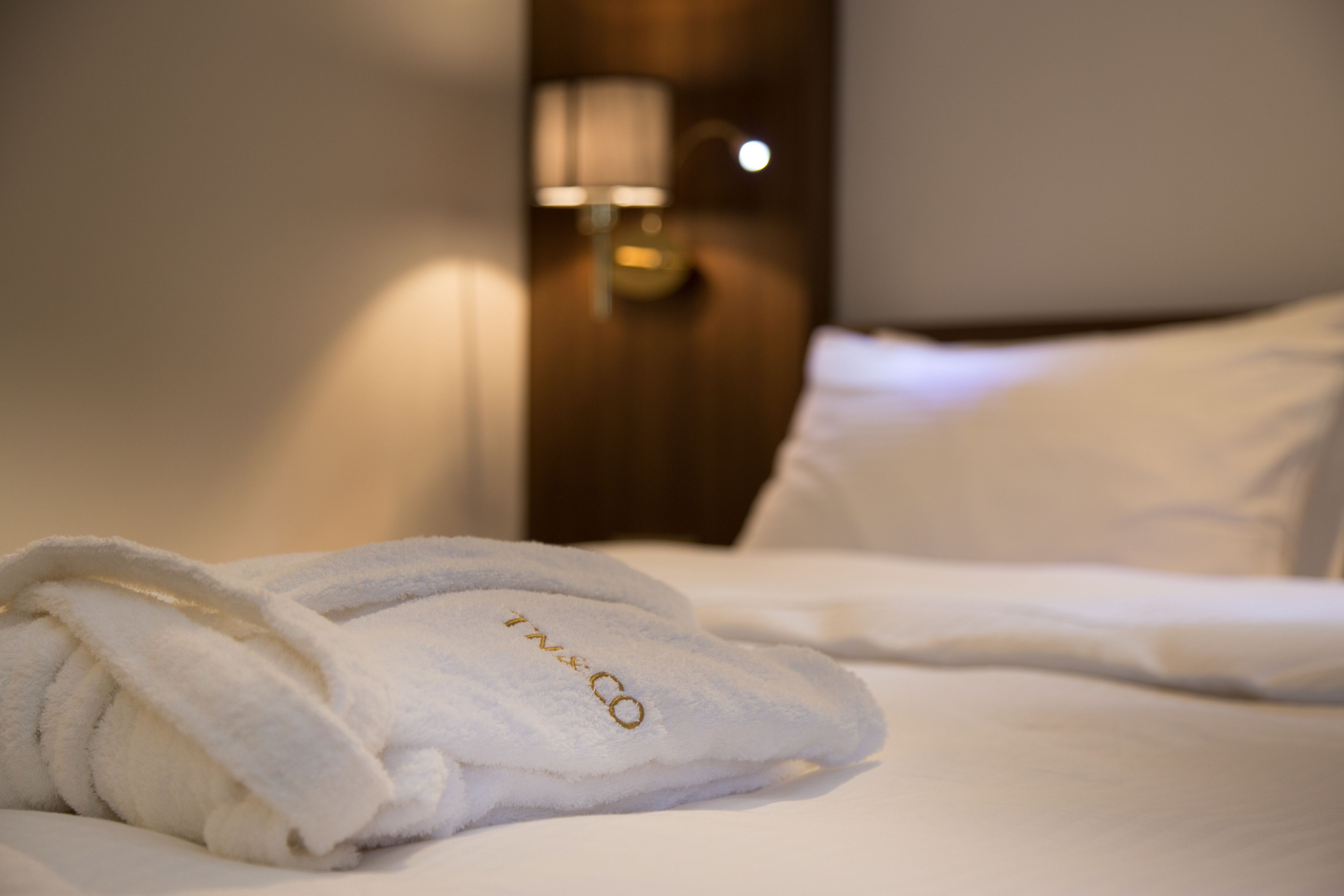 Una cama bien hecha con sábanas blancas y un albornoz blanco con bordados.
