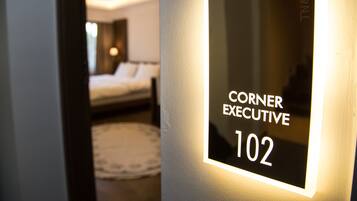 Ein Hotelzimmer mit einem Bett, einem Nachttisch und einem an der Wand befestigten Schild mit der Aufschrift 'Corner Executive 102'.
