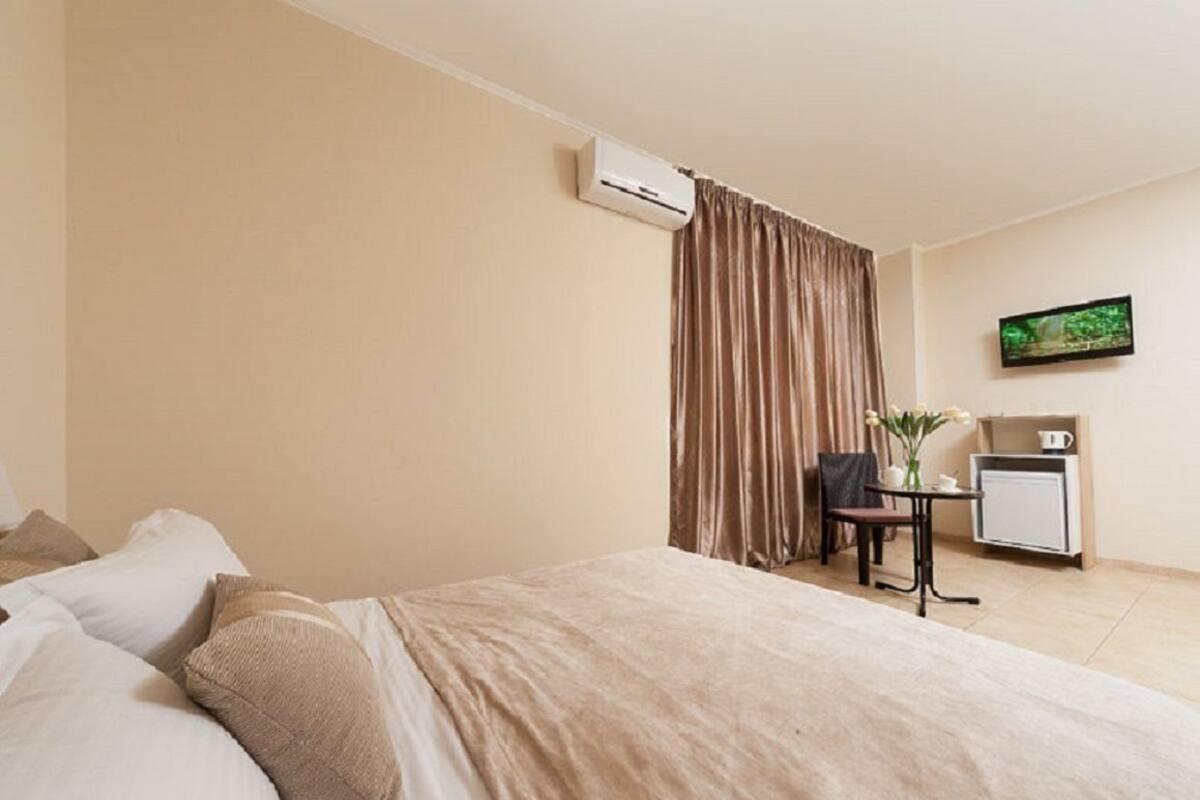 A hotel room with a bed, a small table with a chair, an air conditioning unit, a television, and a radiator.