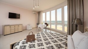 Une chambre d’hôtel avec un lit, un bureau, une chaise, une télévision et une vue sur la plage.