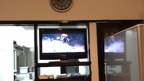 A kitchen with a built-in TV, a clock, and a shelf with various kitchenware. - Condominium Seafront Moon and Sand (Ito)