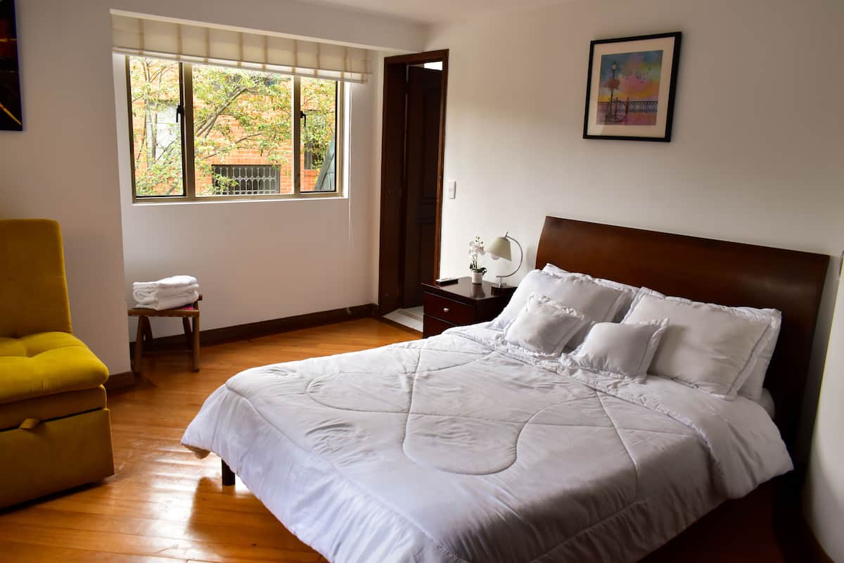 A bedroom with a large bed, a chair, a window, and a painting on the wall.
