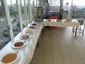 A buffet setup with various dishes on a long table, a food display case, and a view of the outside through large windows. - Wan Jin Hot Spring (New Taipei City)