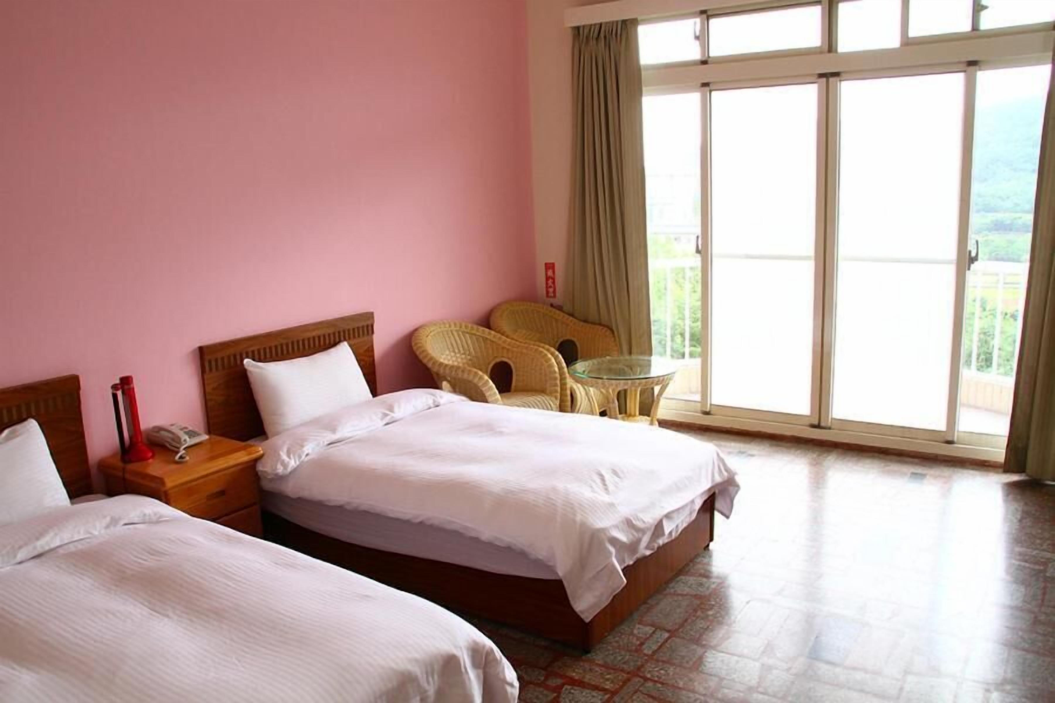 A hotel room with two beds, a small table, and a chair.