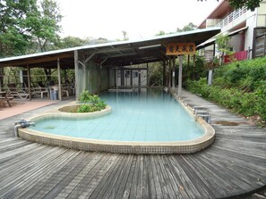 A swimming pool with a wooden deck, a covered seating area, and a sign in a foreign language. - Wan Jin Hot Spring (New Taipei City)
