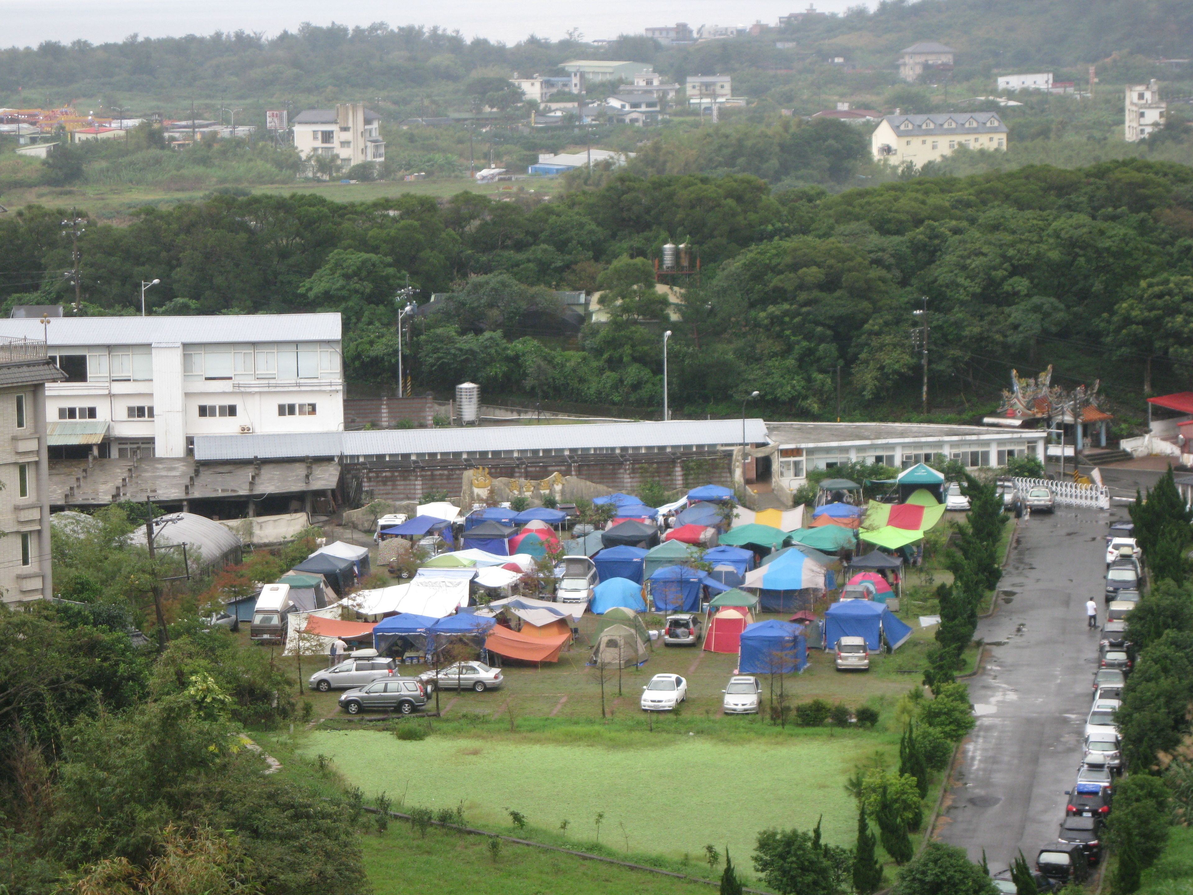 A parking lot with several tents and cars.