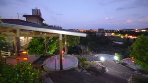 A covered outdoor area with a circular water feature, a pathway, and a view of a distant cityscape at dusk. - Wan Jin Hot Spring (New Taipei City)