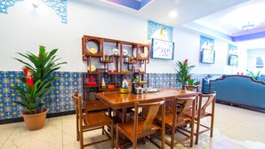 A dining area with a wooden table and chairs, a decorative shelf with plates and bowls, and a blue tiled wall with a patterned border. - Hotel Hilal (Cyberjaya)