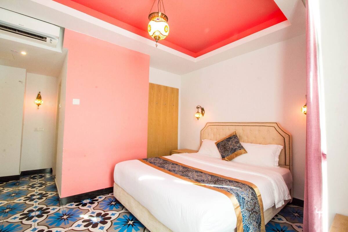 A hotel room with a bed, a wooden headboard, a patterned floor, and a red ceiling.