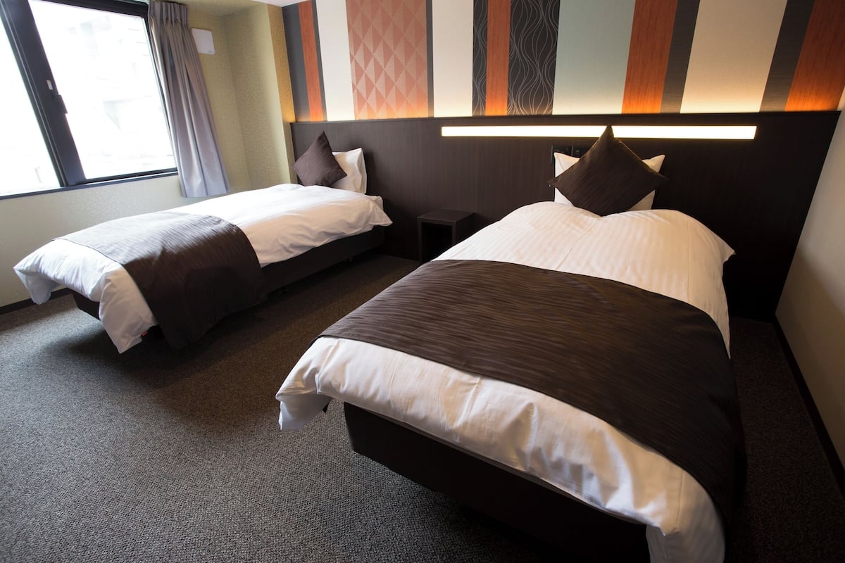 Une chambre d’hôtel avec deux lits, une petite table et une fenêtre avec des rideaux.