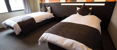 Habitación de hotel con dos camas, una mesita y un ventanal con cortinas.