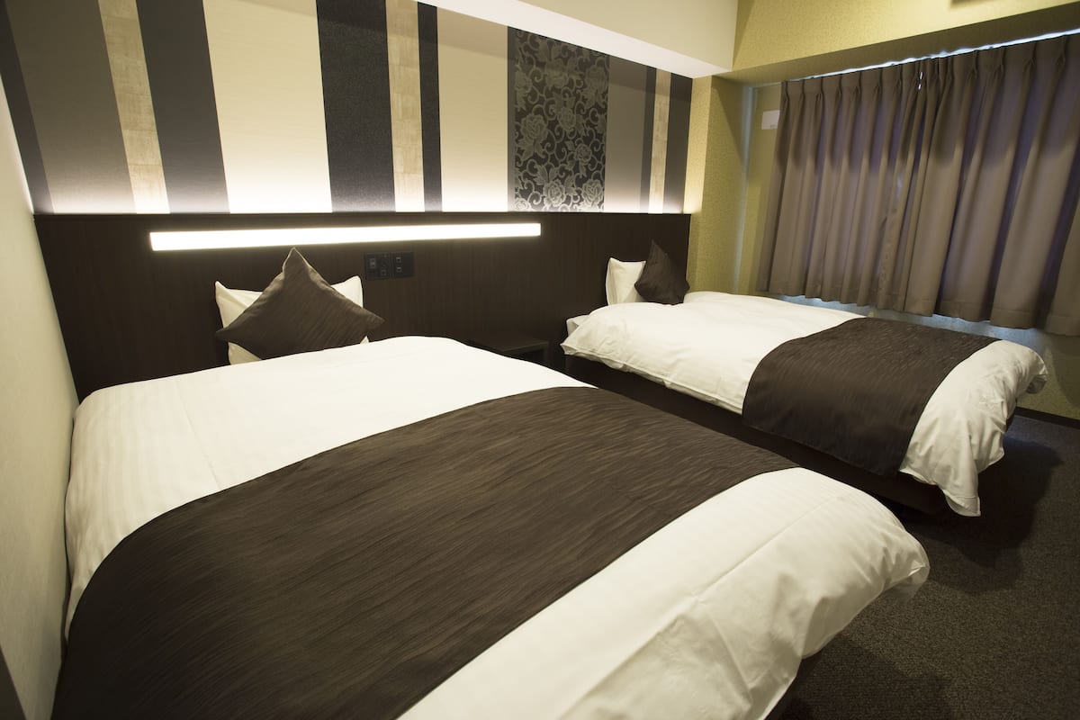 Une chambre d’hôtel avec deux lits, une tête de lit dotée d’une bande lumineuse et un rideau à la fenêtre.