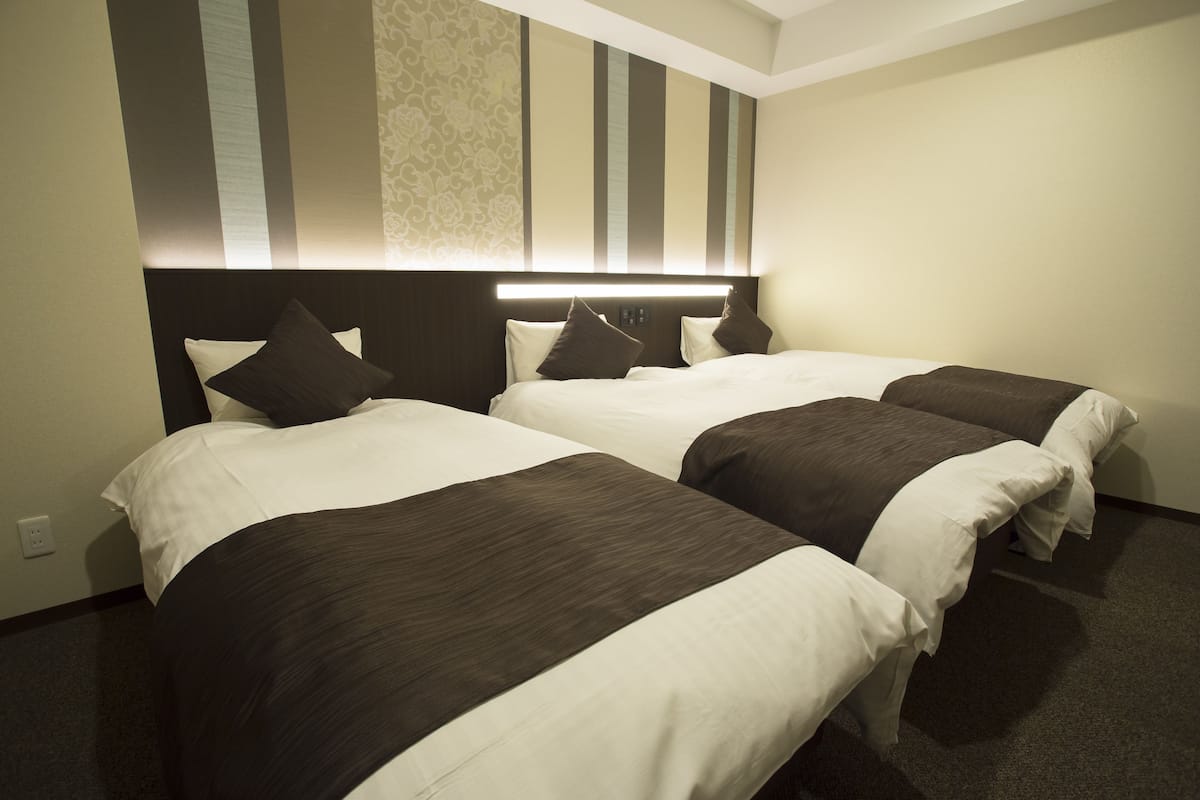 Une chambre d’hôtel avec deux lits, une tête de lit dotée d’un éclairage intégré et un mur orné d’un motif.