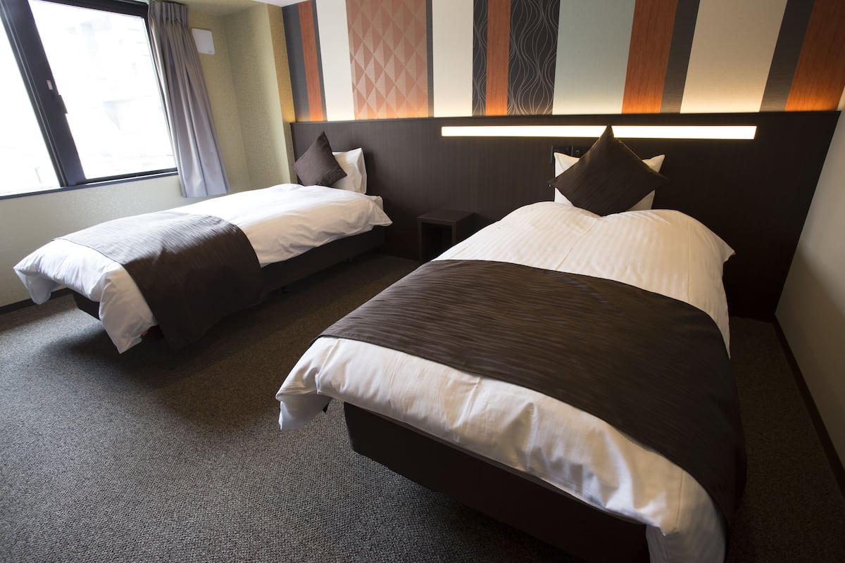 Une chambre d’hôtel avec deux lits, une table de chevet et une fenêtre avec des rideaux.