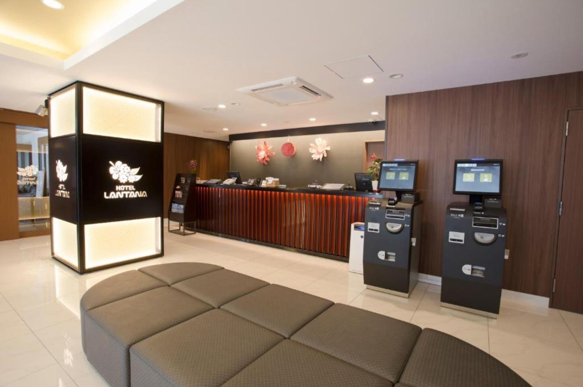 A hotel reception area with a modern design, including a reception desk, seating area, and self-service kiosks.