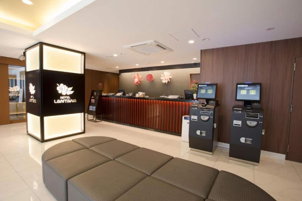 Un espace d’accueil d’hôtel au design moderne, comprenant un comptoir d’accueil, un espace salon et des bornes en libre-service.