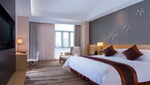 Quarto de hotel com uma cama grande, uma escrivaninha com cadeira, televisão e janela com cortinas.