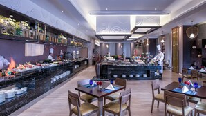 Um restaurante moderno com um balcão extenso, várias mesas e um chef a preparar comida.