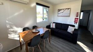 A compact living space with a dining table, chairs, a black sofa, and a window. - Mandurah Coastal Holiday Park (Mandurah)