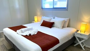 A neatly made bed with white and red linens, a remote control, and a bedside lamp on a white nightstand. - Mandurah Coastal Holiday Park (Mandurah)