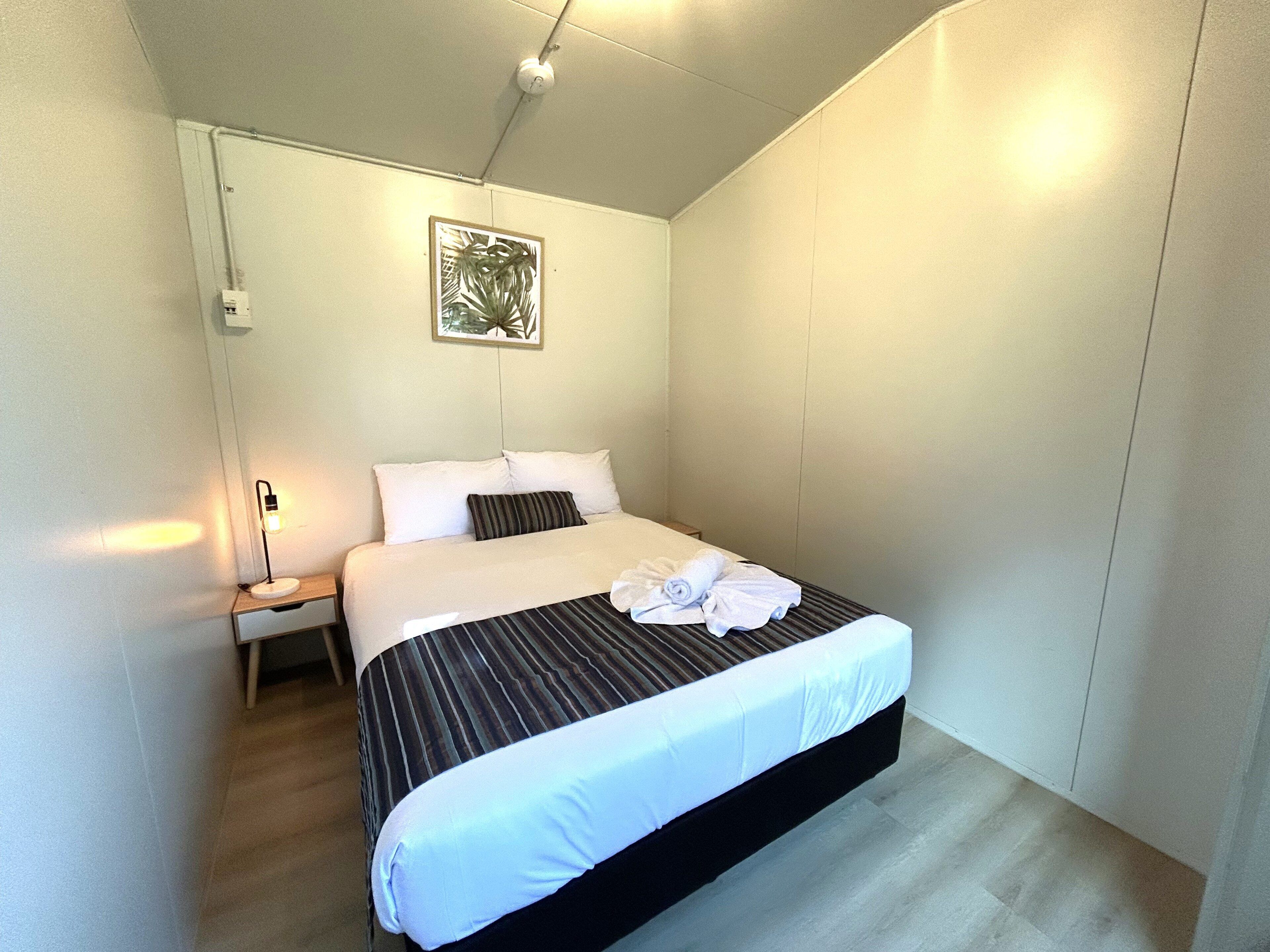 Una cama bien hecha con cubrecama a rayas y ropa de cama blanca, una lámpara de noche y una obra de arte enmarcada en la pared.
