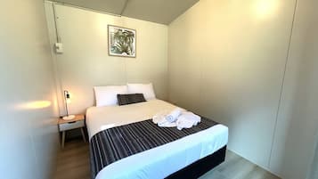 Una cama bien hecha con cubrecama a rayas y ropa de cama blanca, una lámpara de noche y una obra de arte enmarcada en la pared.