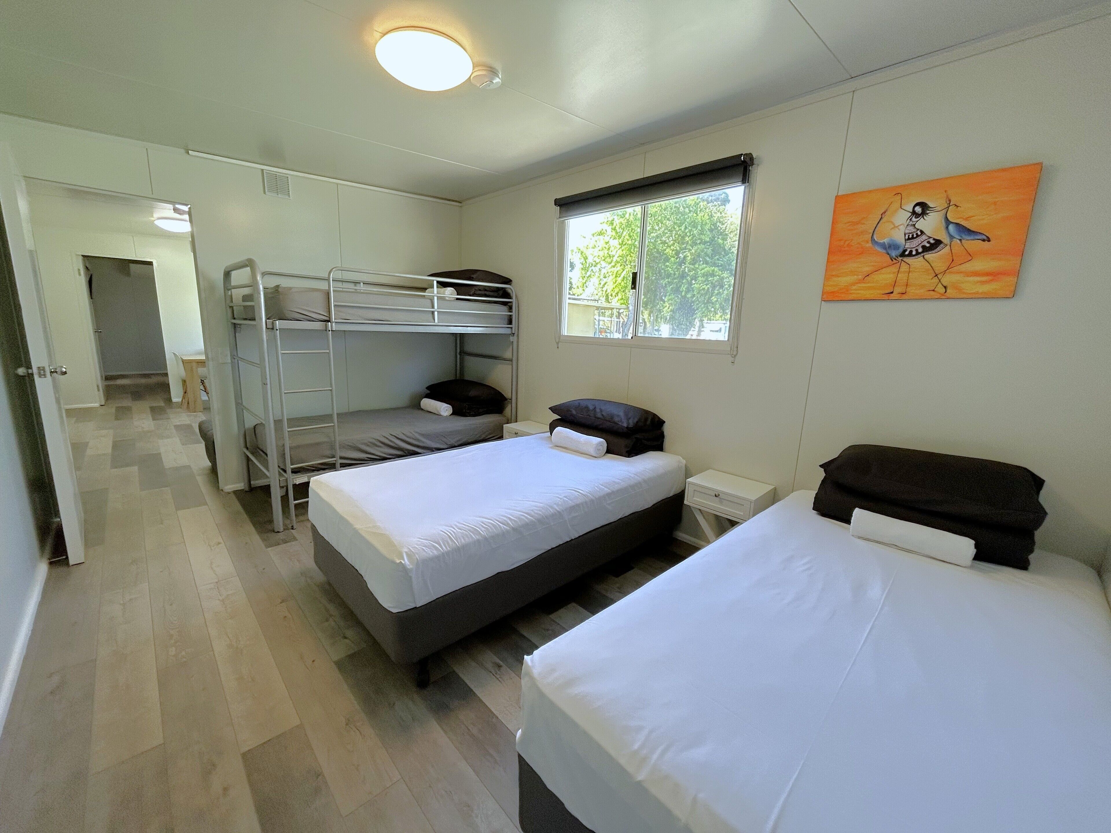 A bedroom with bunk beds, a single bed, a window with a view, and a painting on the wall.