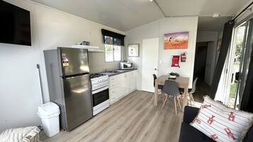 Cocina compacta equipada con refrigerador, estufa, microondas y lavaplatos. Cuenta con un comedor con mesa y sillas, y un área de estar con sofá y ventana.