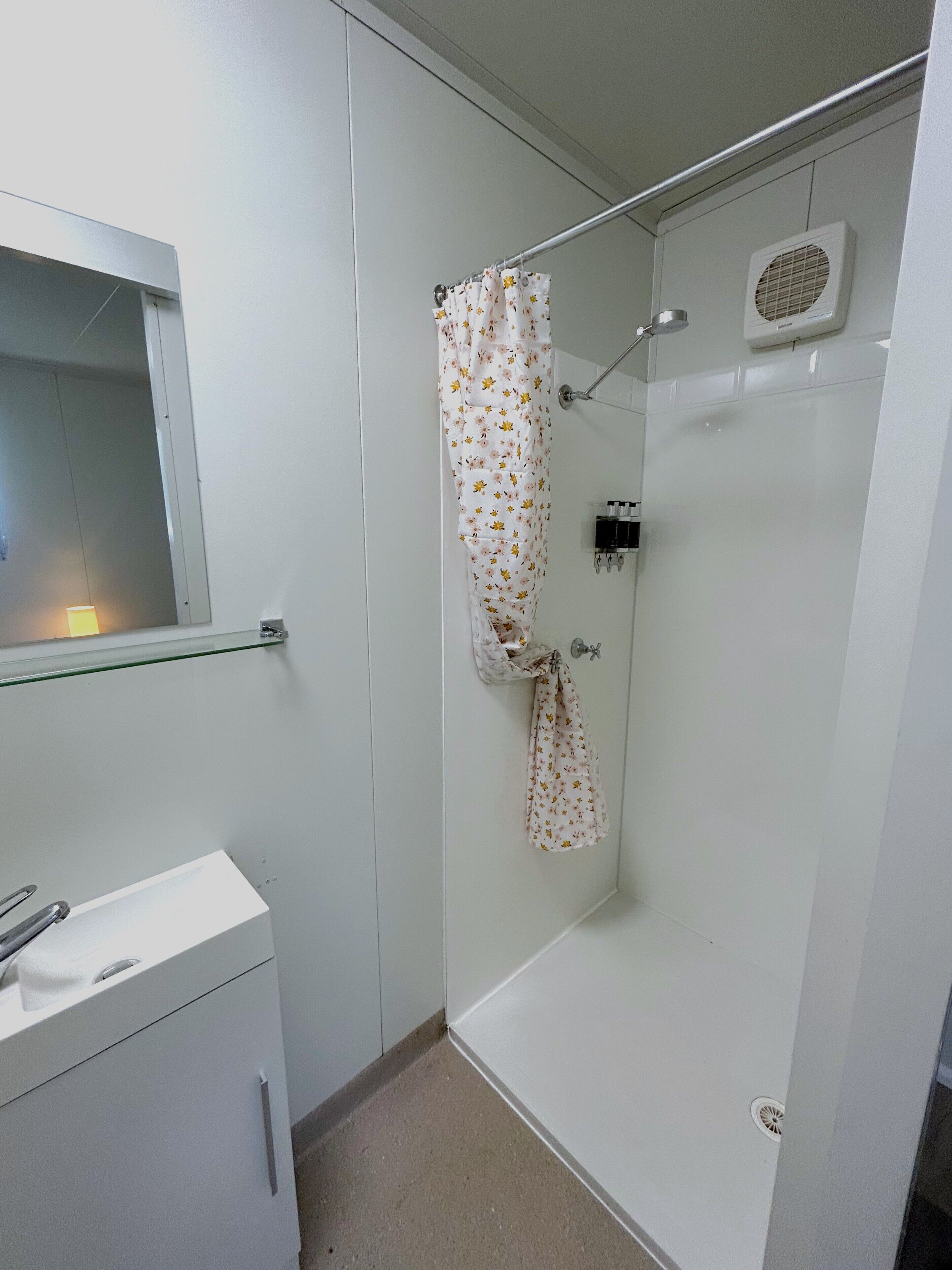 Un baño pequeño y limpio con ducha, espejo y lavamanos.