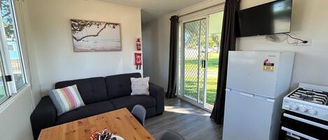 A compact living space with a sofa, a dining table, a refrigerator, a gas stove, a television, and a sliding glass door to the outdoors.