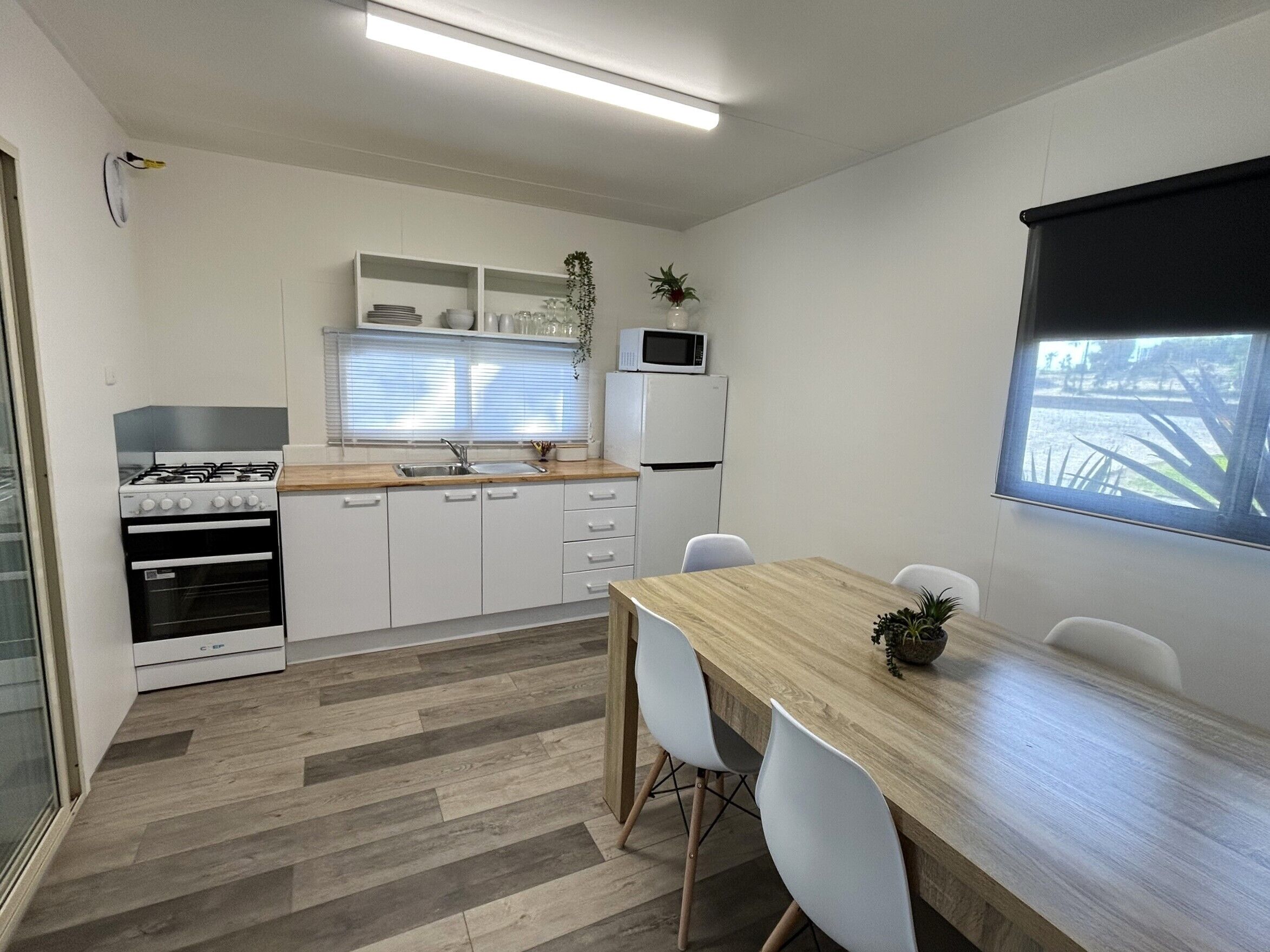A compact kitchen with white cabinets, a wooden countertop, a gas stove, a microwave, and a refrigerator. There is a dining table with chairs and a window with a view of the outdoors.