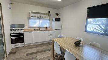 A compact kitchen with white cabinets, a wooden countertop, a gas stove, a microwave, and a refrigerator. There is a dining table with chairs and a window with a view of the outdoors.