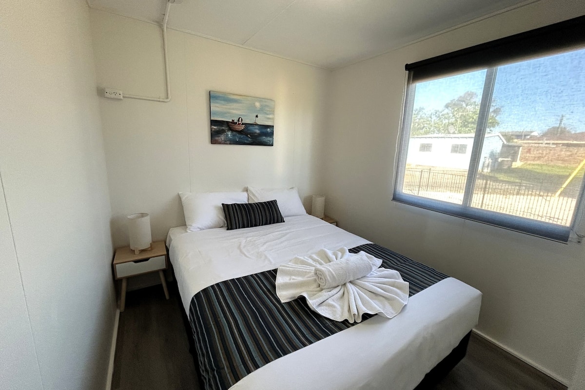 A neatly made bed with striped bedding and a towel, a bedside lamp, and a painting on the wall.