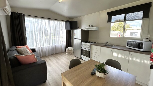 A compact kitchen with a refrigerator, stove, microwave, and a dining area with a table and chairs. - Mandurah Coastal Holiday Park (Mandurah)