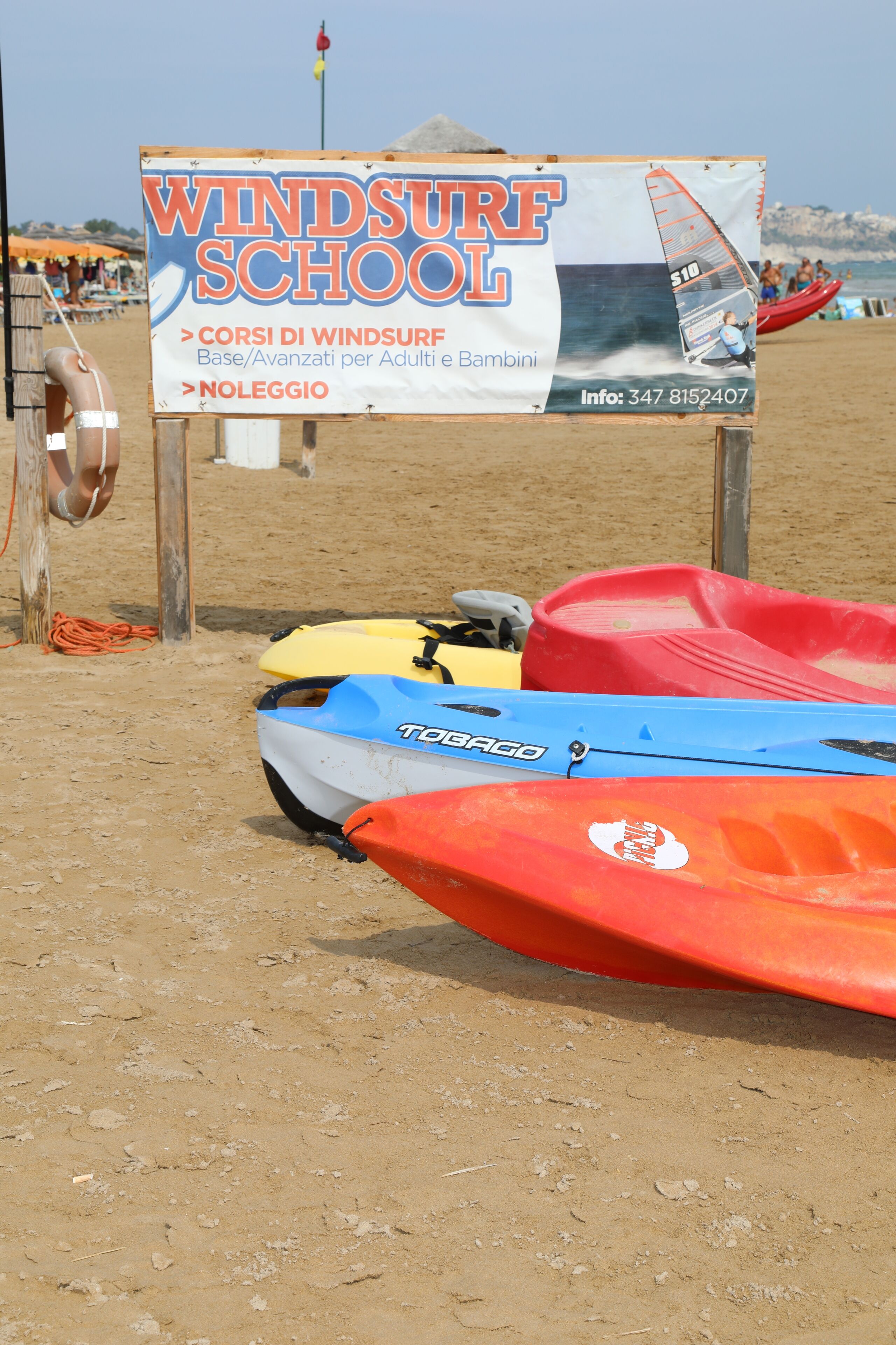 Une plage avec un panneau indiquant une école de planche à voile, qui propose des cours pour adultes et enfants.