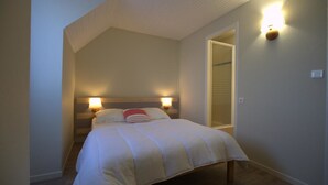 A bedroom with a sloped ceiling, a bed with a striped headboard, two wall-mounted lamps, and a door leading to a closet.