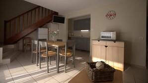 A dining area with a wooden table and chairs, a kitchen with cabinets and a microwave, and a staircase with a TV mounted on the wall.