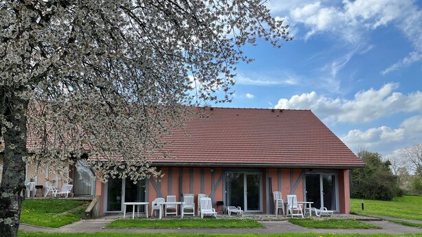A building with a red roof and a covered patio area with white chairs and tables.
