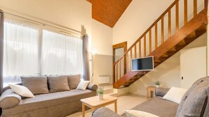 A living room with a sofa set, a coffee table, a TV mounted on the wall, and a wooden staircase.