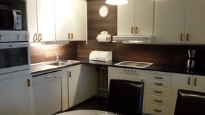 Una cocina moderna con gabinetes blancos, horno empotrado, microondas, cafetera y un reloj en la pared.