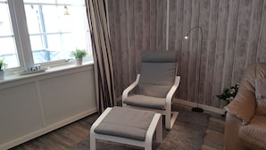 Una sala de estar moderna con un sillón gris, un reposapiés a juego, una lámpara de pie y un sofá color beige.