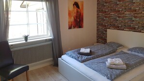 Un dormitorio con dos camas, un radiador, una ventana con cortinas, un cuadro en la pared y un muro con diseño de ladrillos.