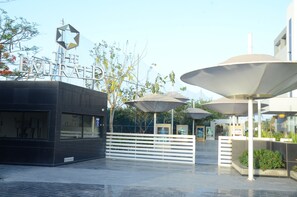 A modern building with a star-shaped sign, outdoor umbrellas, and a white fence. - The Emerald Club (Lodhika)