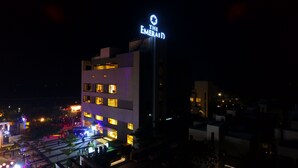 A building with a sign reading "The Emerald." It features multiple floors with windows, and the surrounding area has illuminated structures and people. - The Emerald Club (Lodhika)