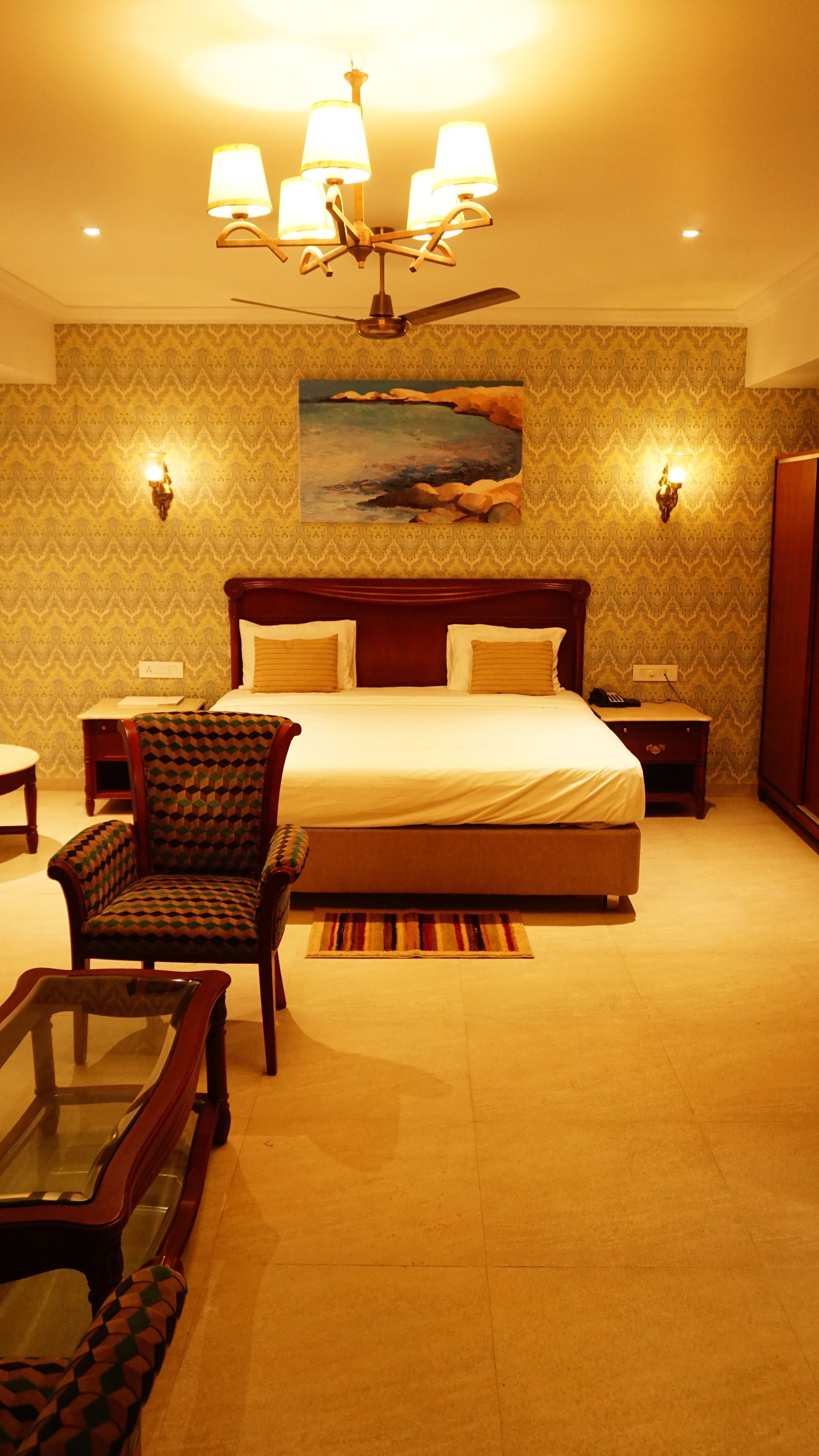 A hotel room with a large bed, a chair, a desk, and a ceiling fan.