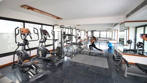 A modern gym with various exercise equipment, large windows, and a spacious layout. - The Emerald Club (Lodhika)